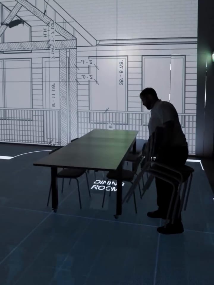 Chairs being set around a dining table on the lit plan, with the elevation screen lit behind
